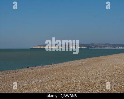 Una scena marina illuminata dal sole a Seaford, guardando attraverso un'ampia spiaggia punteggiata di uccelli e il canale Inglese fino a un promontorio di gesso scogliera attraverso la baia. Foto Stock