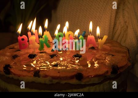 Candele multicolore sotto forma di lettere su una torta di compleanno. Sfondo con spazio di copia. Colorate candele di compleanno felice che bruciano su una torta Foto Stock