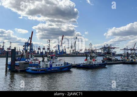 AMBURGO, GERMANIA - 19 MARZO 2022: Nave antincendio Fairplay XV e altri rimorchiatori nel porto di Amburgo. Gru container sullo sfondo. Foto Stock