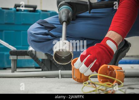 Perforazione di scatole di prese elettriche in pareti di cemento utilizzando potenti attrezzature di perforazione. Elettricista al lavoro. Foto Stock