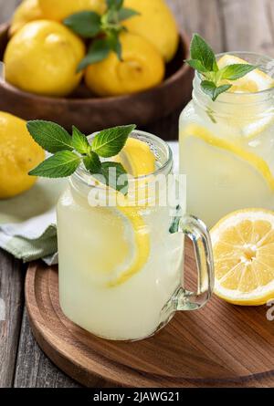 Due bicchieri di limonata con menta e limone su un vassoio di legno con ciotola di limoni sullo sfondo Foto Stock