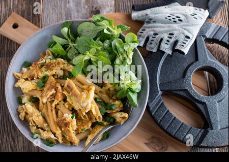 Pasto fitness con pasta di grano integrale fritta in padella e uova strapazzate. Servito con un manubbell su un tavolo di legno. Vista dall'alto Foto Stock