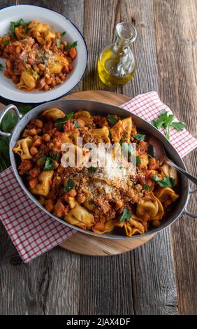 Piatto di pasta italiana con tortellini, pancetta, ceci, verdure e salsa di pomodoro. Condito con parmigiano e servito in una padella rustica Foto Stock