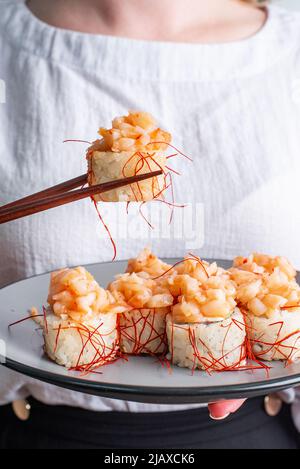 la ragazza tiene un piatto e mangia sushi con bacchette Foto Stock