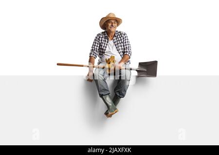 Ritratto a tutta lunghezza di un agricoltore maturo con una lancia seduta su un pannello vuoto isolato su sfondo bianco Foto Stock