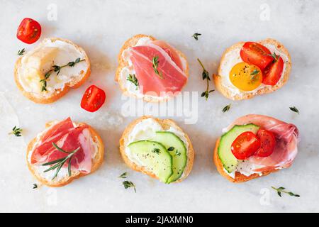 Assortimento di crostini di formaggio cremoso, antipasti con una varietà di condimenti. Vista dall'alto su sfondo di marmo bianco. Concetto di cibo per feste. Foto Stock