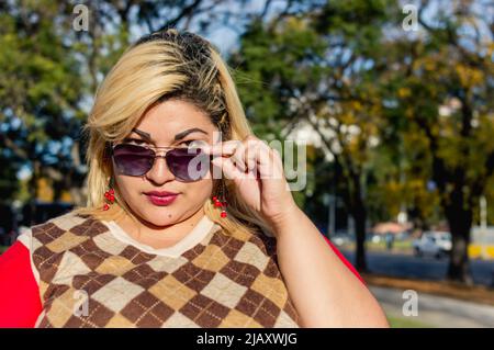 bionda latino argentina giovane donna all'aperto guardando la macchina fotografica sopra i suoi occhiali da sole, stile di vita concetto con spazio copia. Foto Stock