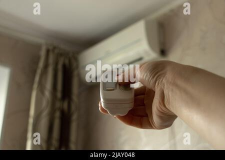 Il telecomando dal condizionatore d'aria nella mano della ragazza è diretto al condizionatore d'aria nell'appartamento, accendere il condizionatore d'aria, clima Foto Stock