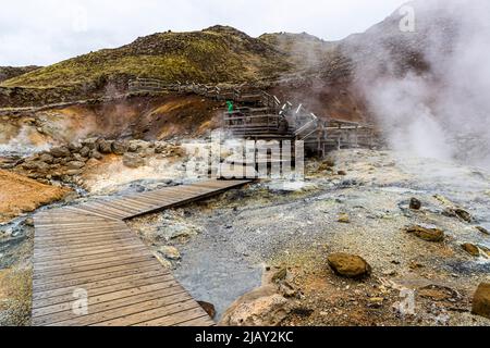 Una passerella di legno con una piattaforma panoramica attraversa l'area geotermica di Seltún vicino a Krýsuvík nella penisola di Reykjanes, in Islanda, passando davanti a fumarole fumanti e rocce macchiate di minerali. Foto Stock