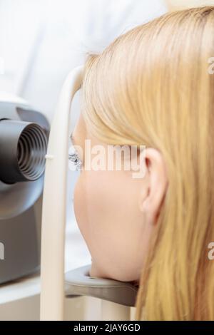 Una giovane ragazza alla reception dell'oftalmologo controlla la vista su un apparecchio speciale. Primo piano. Foto Stock