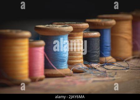 Sette vecchie bobine di filo di legno in diversi colori in stile retrò e vintage in tenue luce contrastata Foto Stock