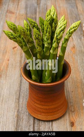 un mazzo di asparagi in una pentola di ceramica su sfondo di legno Foto Stock