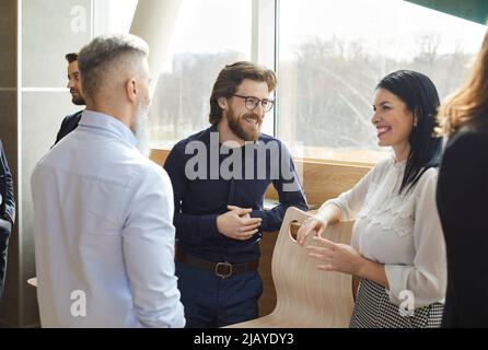 Colleghi di lavoro che si divertono a chattare e a discutere di lavoro in una conversazione casuale in ufficio. Foto Stock