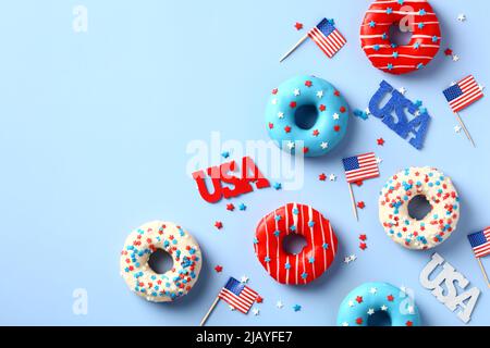 Happy Independence Day USA. Composizione piatta con ciambelle, bandiere americane, decorazioni su sfondo blu. Foto Stock