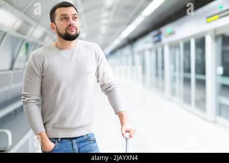 Giovane uomo in piedi con valigia sulla piattaforma della stazione della metropolitana Foto Stock