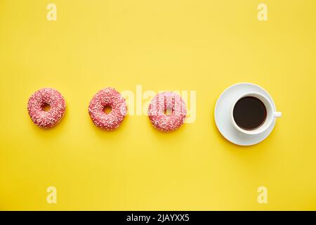 Tazza di caffè nero e ciambelle rosa con spruzzi in linea su sfondo giallo, concetto calorie Foto Stock