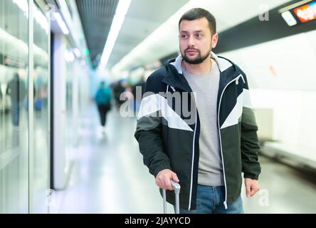 Giovane uomo in piedi con valigia sulla piattaforma della stazione della metropolitana Foto Stock