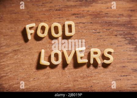 Texte sur Food Lovers formò con lettere alfabetiche sulla pasta della zuppa su sfondo di legno. Foto Stock