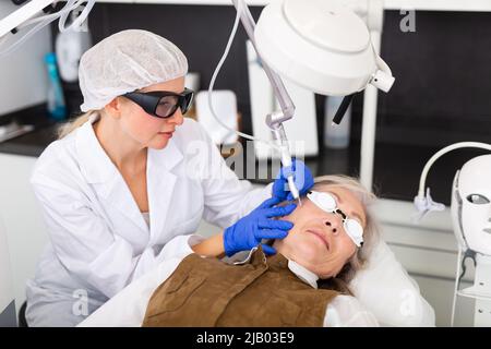 Cosmetologo che usa il laser per rifare la pelle del volto della donna matura Foto Stock