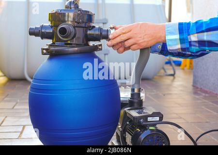 Pool cleaning equipment.Blue filtro acqua nelle mani di un uomo in una camicia blu sul terrazzo vicino alla casa.man muove i tubi al filtro in Foto Stock