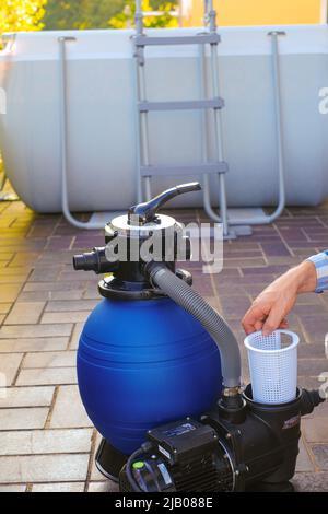 Filtro pool. Attrezzatura per la pulizia della piscina. Filtro dell'acqua nelle mani di un uomo sulla terrazza vicino alla casa.l'uomo muove i tubi al filtro in Foto Stock