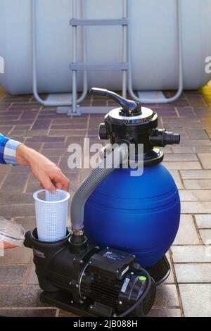 Filtro pool. Attrezzatura per la pulizia della piscina. Filtro dell'acqua nelle mani di un uomo sulla terrazza vicino alla casa.l'uomo muove i tubi al filtro in Foto Stock