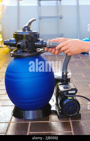 Pool cleaning equipment.Blue filtro acqua nelle mani di un uomo in una camicia blu sul terrazzo vicino alla casa.man muove i tubi al filtro in Foto Stock