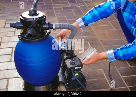 Filtro pool. Piscina pulizia equipment.Blue filtro acqua nelle mani di un uomo in una camicia blu sul terrazzo vicino alla casa.man muove i tubi Foto Stock