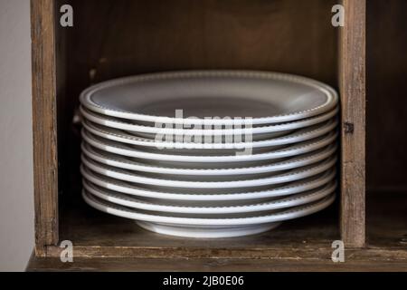 Una pila di piatti da pranzo in porcellana bianca in un armadietto di legno in una casa o in un ristorante Foto Stock