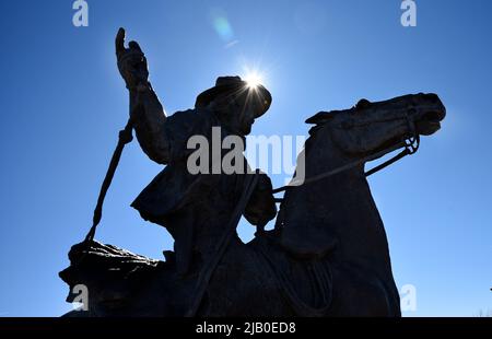 Una scultura in bronzo di un cowboy a cavallo si staglia contro il sole del pomeriggio a Santa Fe, New Mexico. Foto Stock