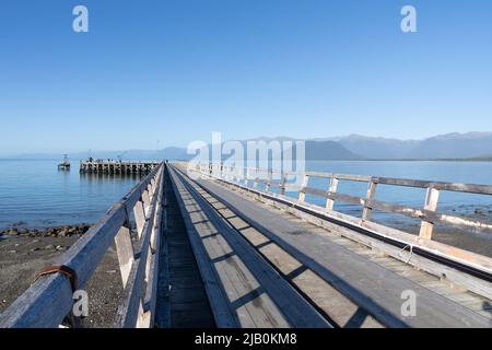 Jackson Bay New Zealand - Aprile 27 2022; lunghe linee e ombre del molo che si proiettano nella baia sotto il cielo blu. Foto Stock