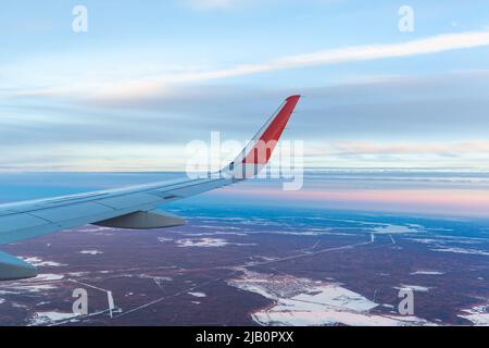 Volo in aereo al tramonto o all'alba. L'ala e la terra dell'aeromobile sono visibili attraverso l'illuminatore. Vista dalla finestra del piano. Aereo, aereo. Traversata Foto Stock