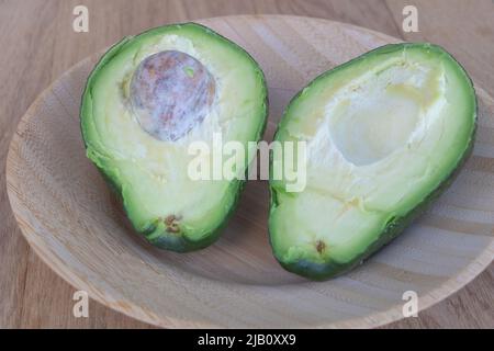 Primo piano girato un avocado tagliato a metà su un piatto di legno - vantaggi del concetto di avocado Foto Stock