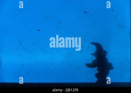 Ombre notturne sulla parete blu. Silhouette nera di uno stargazer in miniatura su una parete macchiata ruvida. Profilo di un vecchio barbuto in un cappello a punta. Sele Foto Stock
