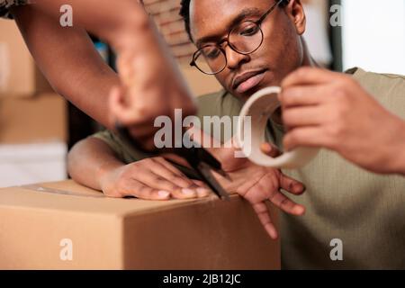 African american People sigillare scatole di cartone con nastro adesivo per spostare mobili in nuova proprietà immobiliare. Imballando le cose e il carico di deposito di spedizione, godendo del trasferimento piatto. Primo piano. Foto Stock