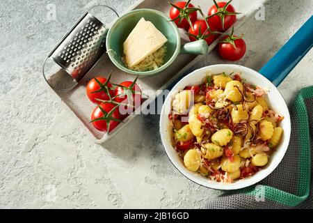 Da sopra di appetitosi gnocchi di patate serviti in padella su tavola di cemento con pomodori freschi e formaggio grattugiato Foto Stock