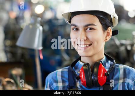 Ritratto di sorridente giovane donna lavoratore in hardhat indossare cuffie rosse sul collo, donna in concetto di industria Foto Stock