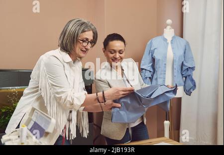 Due marinai al lavoro. Stilisti esperti personalizzano i cassettieri guardando il tessuto, discutendo la qualità del tessuto. Colleghi al cucito moderno Foto Stock