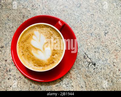 Un caffè bianco piatto in una tazza rossa e un piattino. Arte decorativa del caffè formata nella schiuma del caffè. Foto Stock