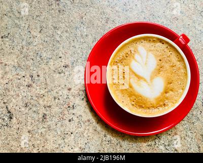 Un caffè bianco piatto in una tazza rossa e un piattino. Arte decorativa del caffè formata nella schiuma del caffè. Foto Stock