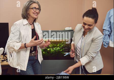 Allegri designer di moda sul posto di lavoro in un atelier di design e sartoria moda. Marinai, sarti, fogne, cassettiere con oggetti da cucire in clo Foto Stock