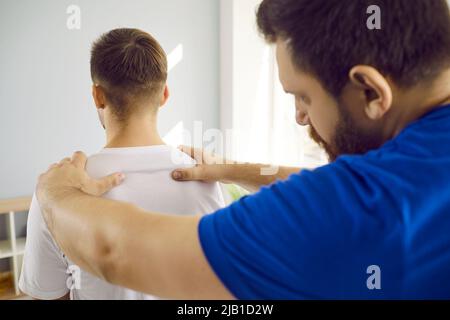 Terapista maschile esperto che esamina la schiena del giovane uomo e nomina il trattamento fisioterapico. Foto Stock