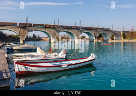 Peschiera del Garda, Italia - 25 marzo 2022: Treno merci cargo su un ponte sul fiume Mincio a Peschiera del Garda, Italia. Foto Stock