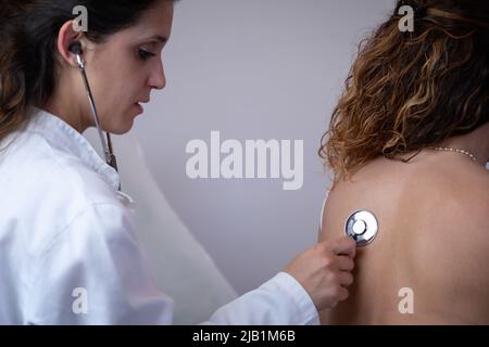 Il medico ascolta il petto del paziente con uno stetoscopio, osservando la respirazione e i rumori interni dell'organismo. Visita medica tradizionale Foto Stock