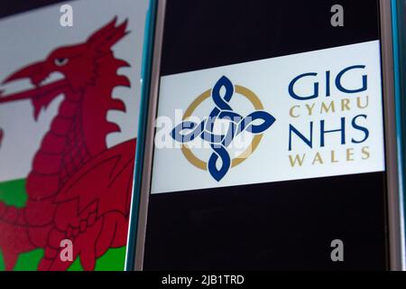 Kumamoto, GIAPPONE - Sep 6 2021 : logo closeup di NHS Wales (gallese: GIG Cymru), il sistema sanitario finanziato pubblicamente in Galles, su iPhone sulla bandiera gallese. Foto Stock