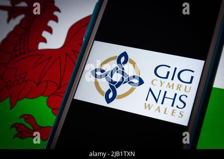 Kumamoto, GIAPPONE - Sep 6 2021 : logo closeup di NHS Wales (gallese: GIG Cymru), il sistema sanitario finanziato pubblicamente in Galles, su iPhone sulla bandiera gallese. Foto Stock