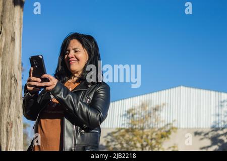 latino caucasica donna adulta fuori in una fattoria utilizzando il telefono sorridente e comunicante con il manager aziendale, concetto di settore, spazio copia. Foto Stock