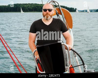 bella persona bearded barca a vela volante su un lago in una nuvolosa giornata estiva Foto Stock