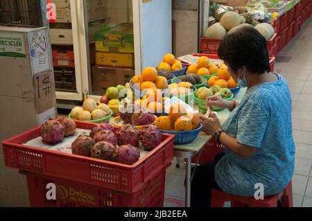 Donna arrangiante prodotti, esposti per la vendita al mercato a Tiong Bahru, Singapore Foto Stock