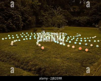 Un modello di lampade rotonde di diversi colori sul prato verde estivo serale. Decorazioni chiare nel parco Foto Stock